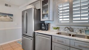 A modern kitchen with stainless steel appliances, a built-in coffee maker, and a marble countertop. - 672 Amelia By The Sea (Fernandina Beach)