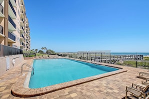 Piscina con vista sull'oceano, circondata da una recinzione e lettini.