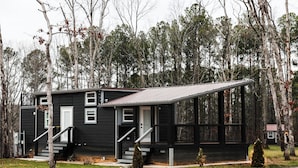 A black cabin with a metal roof, a front porch, and a staircase leading to the entrance. - Pepper's Place 131 ITP (Dover)