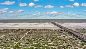 A beach with a wooden pier extending into the ocean, sandy dunes, and a clear sky. - 7th Floor, Corner Property on the top Floor With Easy Beach Access Exclusive Fishing Pier (Fernandina Beach)