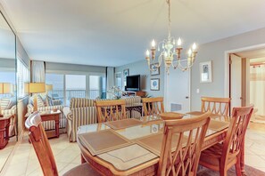 Un vaste espace de vie comprenant une table à manger, des chaises, un lustre et un téléviseur.