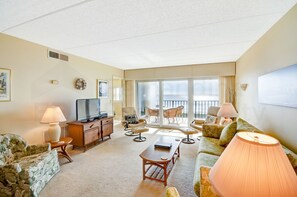 A spacious living room with a television, sofa, chairs, and a balcony with a view. - B4 Amelia South (Fernandina Beach)