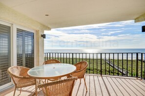 A balcony with wicker furniture and a glass table overlooking a beach and ocean. - B4 Amelia South (Fernandina Beach)