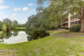 A serene lakeside setting with a building adjacent to the water, surrounded by lush greenery. - Amelia Landings 6C (Fernandina Beach)