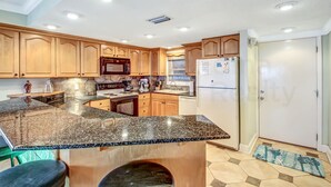 Una cocina moderna con encimeras de granito, armarios de madera y electrodomésticos de acero inoxidable.