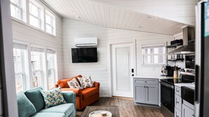 A modern kitchen with white cabinets, a built-in oven, and a microwave. There is a teal sofa with patterned cushions and a coffee table with a tray. - Salt and Pepper at In The Pines Pr6264 (Dover)