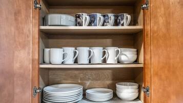 A wooden cabinet with three shelves, each holding white mugs, bowls, and plates.