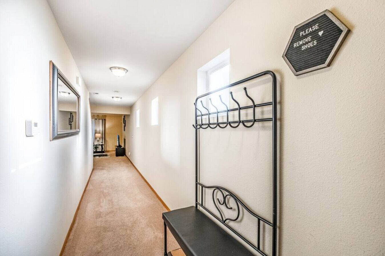 A hallway with a metal coat rack, a sign instructing to remove shoes, and a mirror on the wall.