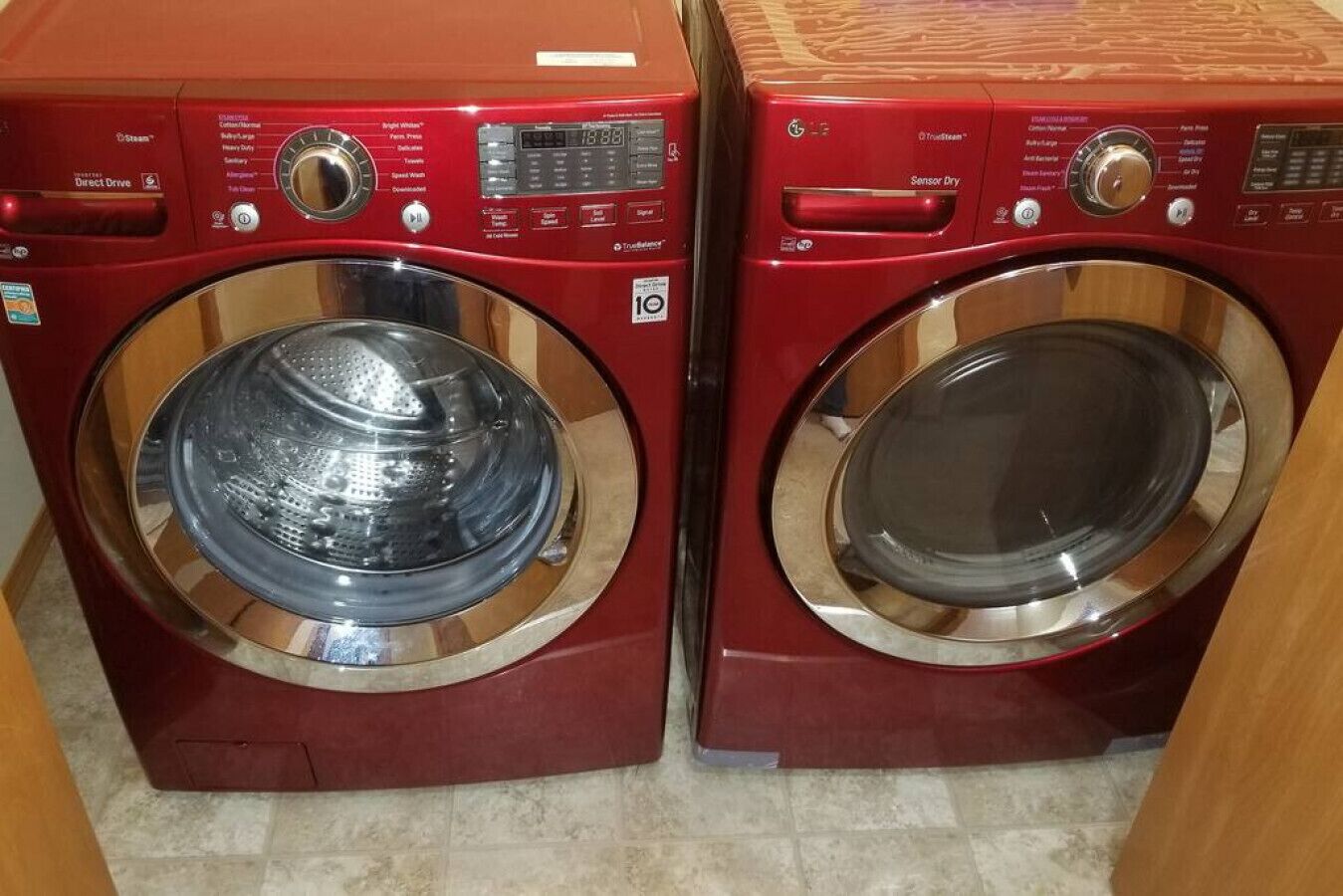 Two red front-loading washing machines with stainless steel doors, control panels, and a "Sensor Dry" label.