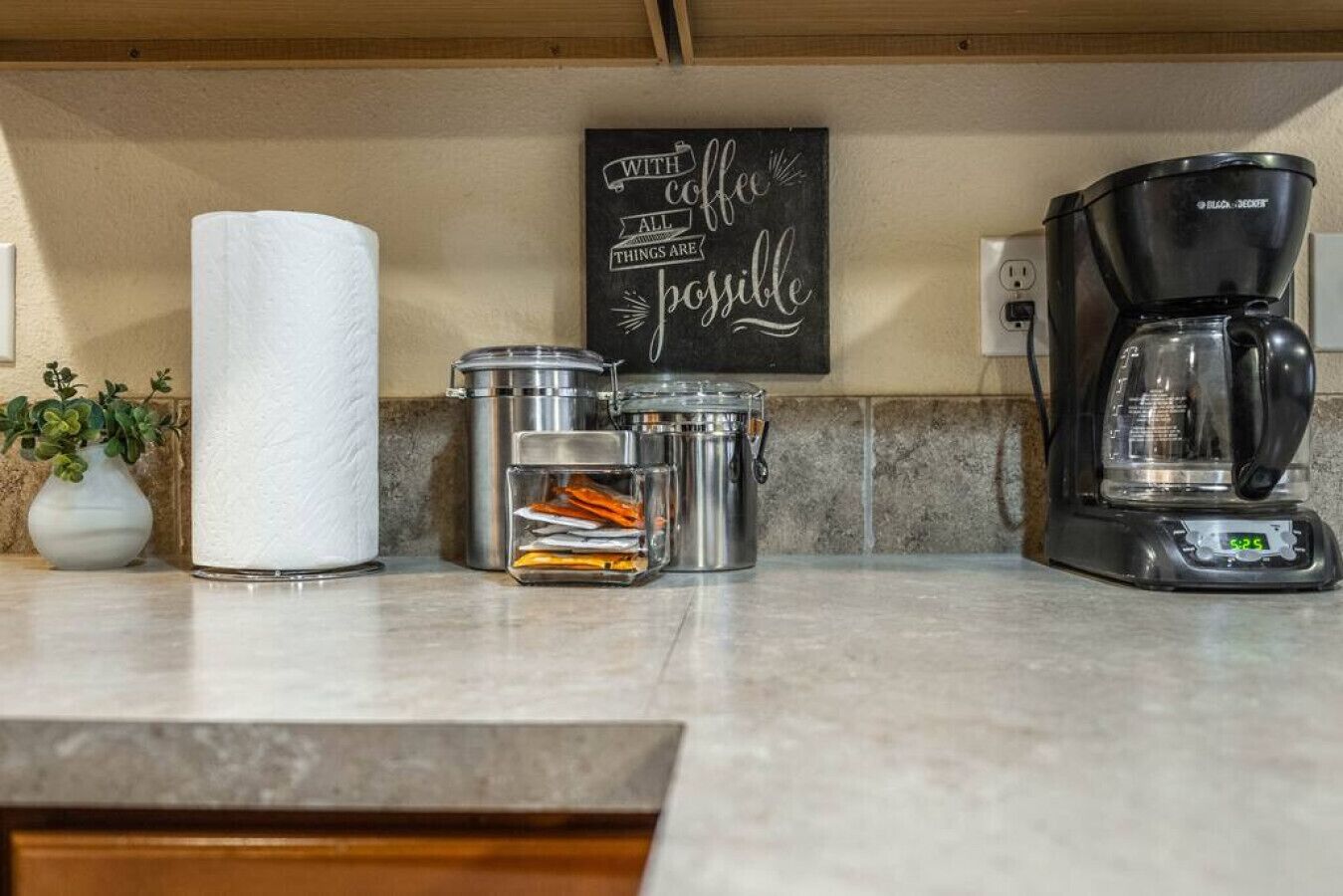 A kitchen counter with a coffee maker, paper towels, and containers.
