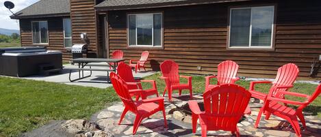 Een houten blokhut met een terras, voorzien van rode Adirondack-stoelen, een barbecue en een vloer van natuursteen.