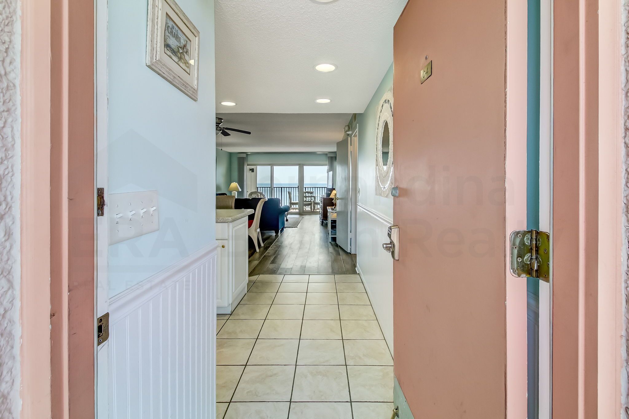 A hallway with a view to a balcony, a ceiling fan, and a door with a mirror.