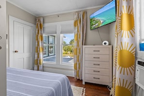 A bedroom with a bed, a TV, a dresser, and a window with curtains. - The Porch at Fort Pierce (Fort Pierce)