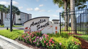 Señal para el condominio Amelia South, con entrada vigilada, palmeras y cielo despejado.