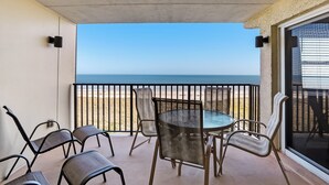 Un balcón con mesa y sillas de vidrio, con vista a una playa.