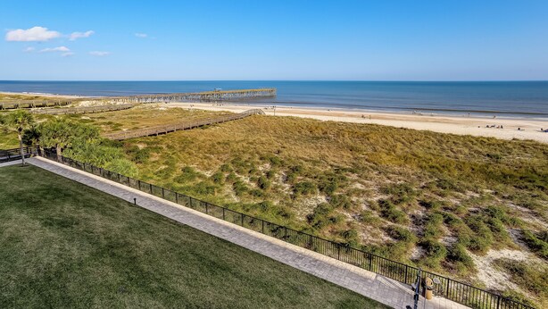 Vista costera con playa, muelle y zona verde con valla.