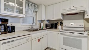 Una cocina con armarios blancos, microondas, horno y lavavajillas.