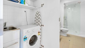 Une petite salle de bain équipée d’un lave-linge, de toilettes et d’un espace douche.