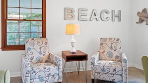 Et værelse med to møblerede lænestole, et lille bord med en lampe, og en væg hvor ordet "BEACH" er stavet med bogstaver.