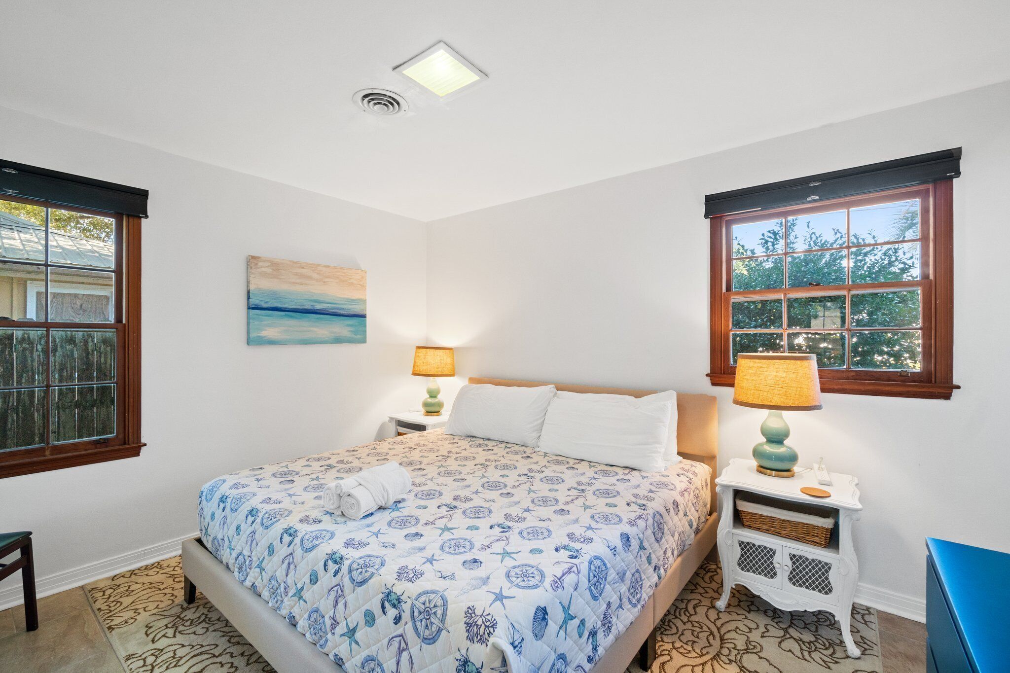 Un dormitorio con una cama, dos mesitas de noche, una lámpara, un cuadro y una ventana.