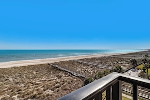 A beach view from a balcony with a wooden walkway leading to the shore, sandy beach, and clear blue sky. - C5 Amelia South (Fernandina Beach)