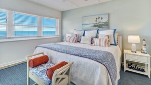 A bedroom with a bed, a chair, a nightstand, a lamp, and a painting on the wall. - C5 Amelia South (Fernandina Beach)