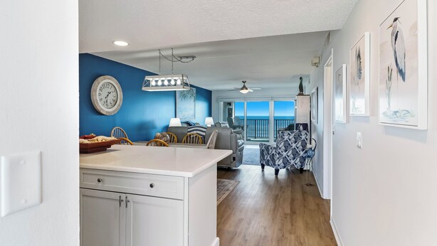 A modern kitchen with white cabinets, a dining area with a blue wall, and a view of the ocean through large windows. - C5 Amelia South (Fernandina Beach)