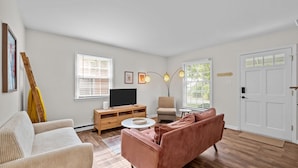 Een woonkamer met een bank, fauteuil, tv-meubel en een deur met een 'WELCOME'-bord.
