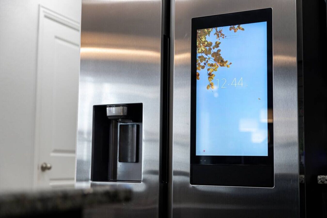 A stainless steel refrigerator with a digital display showing the time and a small compartment with a bottle.