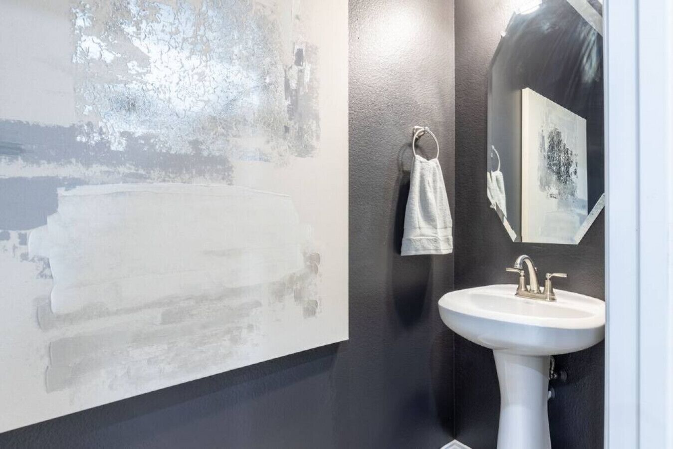 A bathroom with a white sink, a towel ring, and a large abstract painting on the wall.