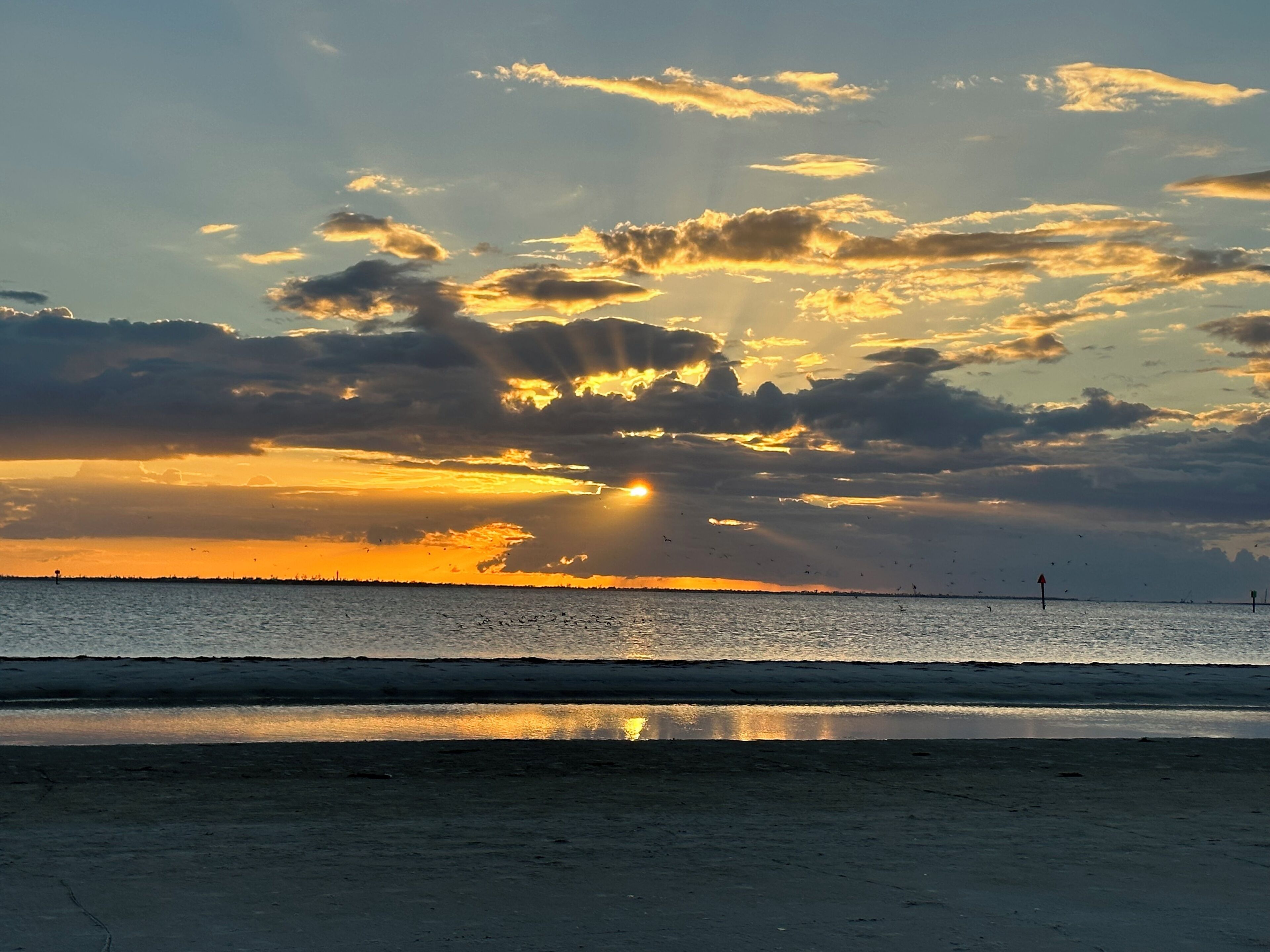 A beach with a sunset, calm water, and a distant shoreline.