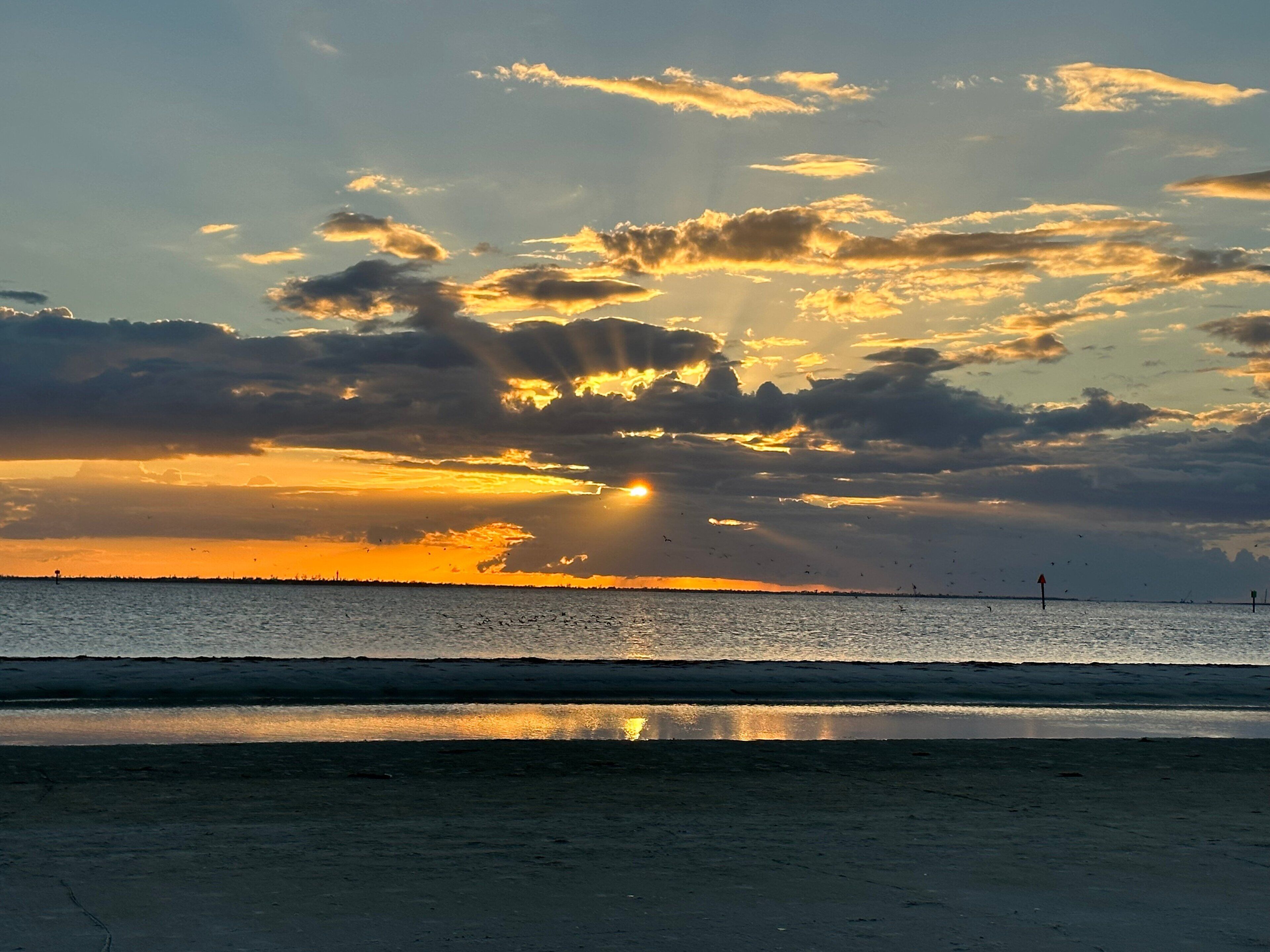 A sunset over a beach with calm waters and a distant shoreline.