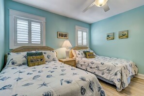 A bedroom with two beds, each with a beach-themed bedspread, a nightstand with a lamp, and two wall-mounted pictures. - E4 Amelia South (Fernandina Beach)