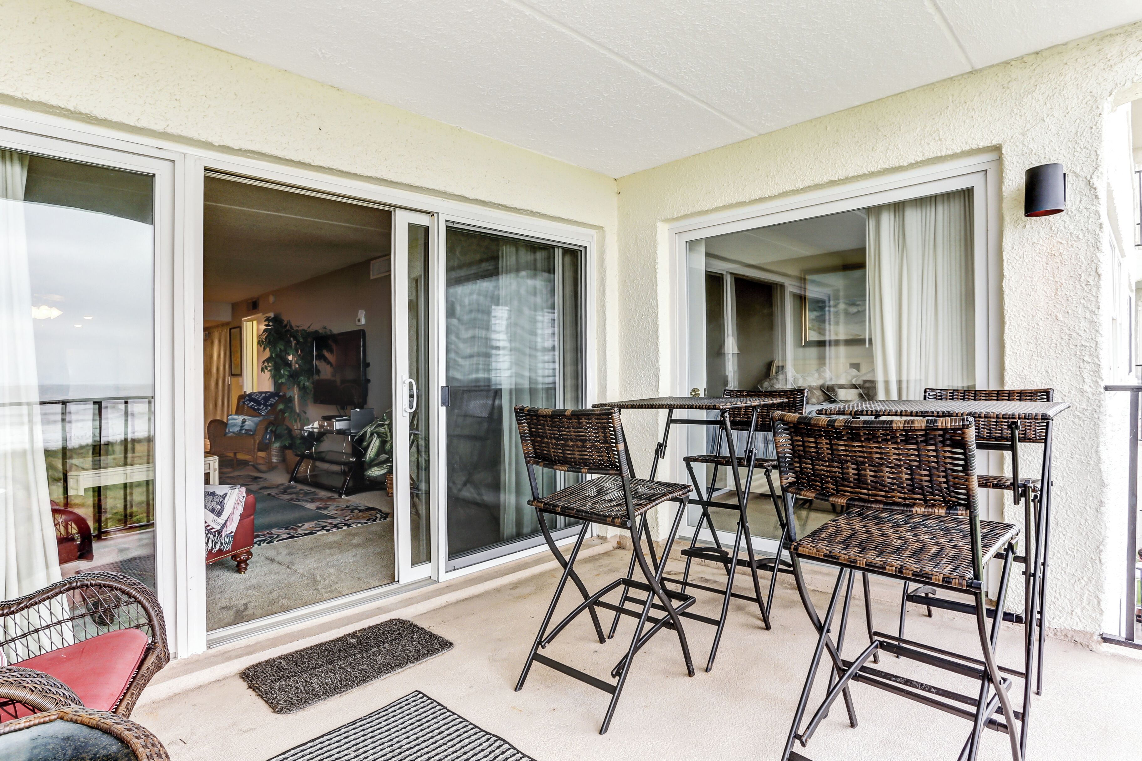 Un balcon avec une table et des chaises, une porte-fenêtre coulissante donnant sur un espace intérieur, et un petit tapis sur le sol.