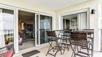 Un balcon avec une table et des chaises, une porte-fenêtre coulissante donnant sur un espace intérieur, et un petit tapis sur le sol.