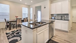 A modern kitchen with white cabinetry, a granite countertop, and a built-in dishwasher. - Charming 3BR Retreat - Perfect for Families! (Fort Collins)
