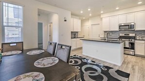 A modern kitchen with white cabinets, a central island, stainless steel appliances, and a dining area with a table set for four. - Charming 3BR Retreat - Perfect for Families! (Fort Collins)