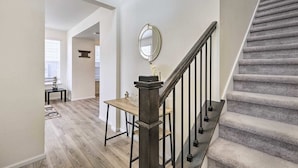 A staircase with a wooden handrail and black balusters, leading to a landing with a round mirror and a small table. - Charming 3BR Retreat - Perfect for Families! (Fort Collins)