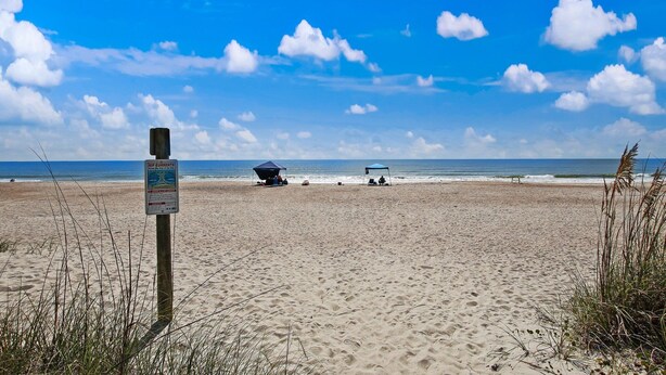Une plage avec un panneau indiquant la présence d’un sauveteur, deux parasols et l’océan en arrière-plan.