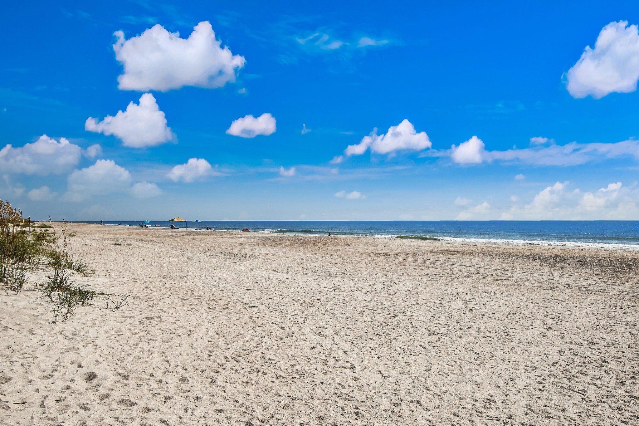 Una amplia playa arenosa con cielo azul despejado y el océano al fondo.