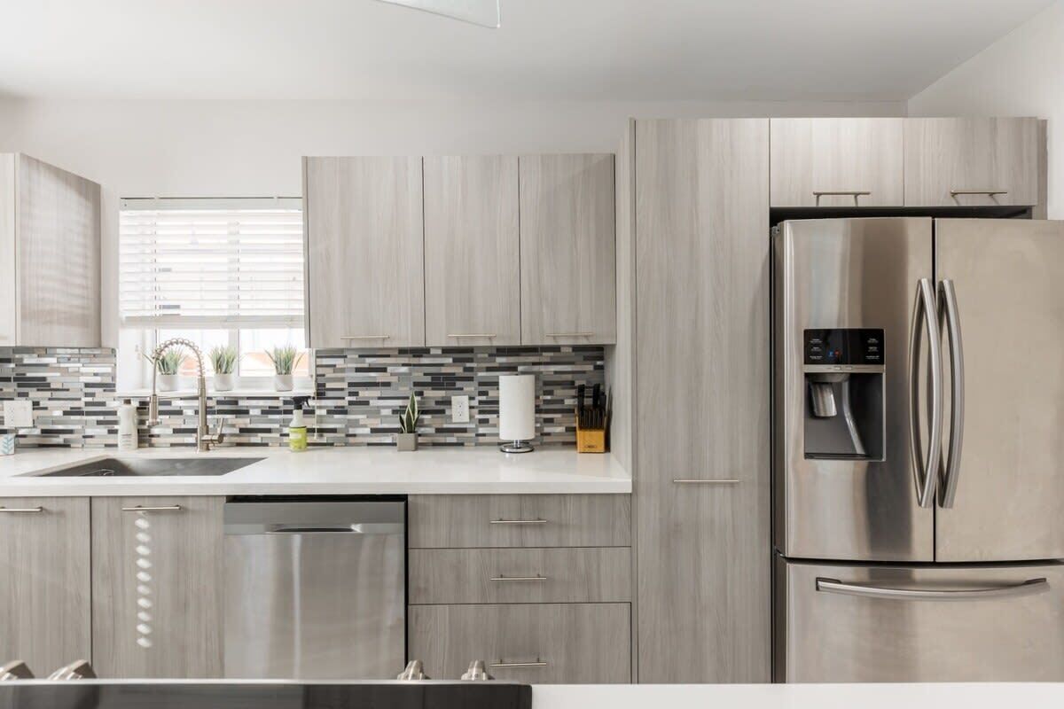 A modern kitchen with a stainless steel refrigerator, grey cabinets, and a tiled backsplash.