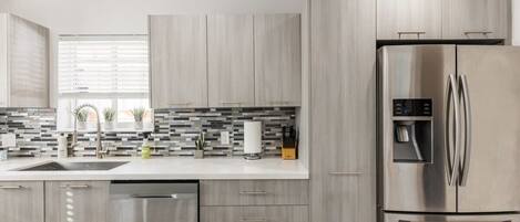 A modern kitchen with a stainless steel refrigerator, grey cabinets, and a tiled backsplash.