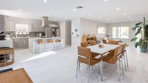 A modern kitchen with a central island, bar stools, and a dining area with a white table and chairs. - Heated Pool & BBQ Olas Villa by Rovetravel (Fort Lauderdale)