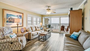 A spacious living room with a ceiling fan, a large painting, and a view to the outside. - M7 Amelia South (Fernandina Beach)