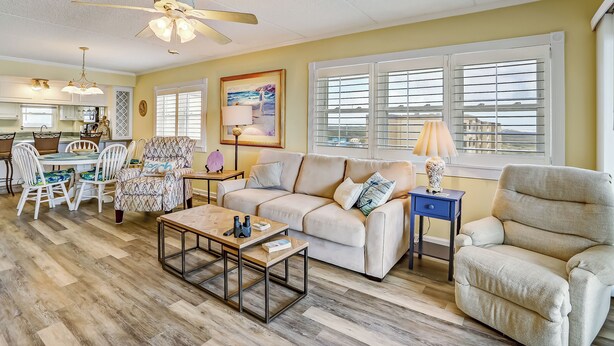 A well-lit living room with a dining area, a ceiling fan, and a large window with blinds. - M7 Amelia South (Fernandina Beach)