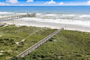 Ein Strand mit einer hölzernen Pier, die sich über den Ozean erstreckt, einer Rasenfläche mit einem Holzsteg und freiem Blick auf das Meer.
