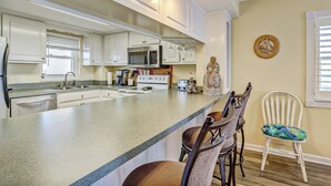 A kitchen with white cabinets, a large island with bar stools, a microwave, and a toaster. - M7 Amelia South (Fernandina Beach)