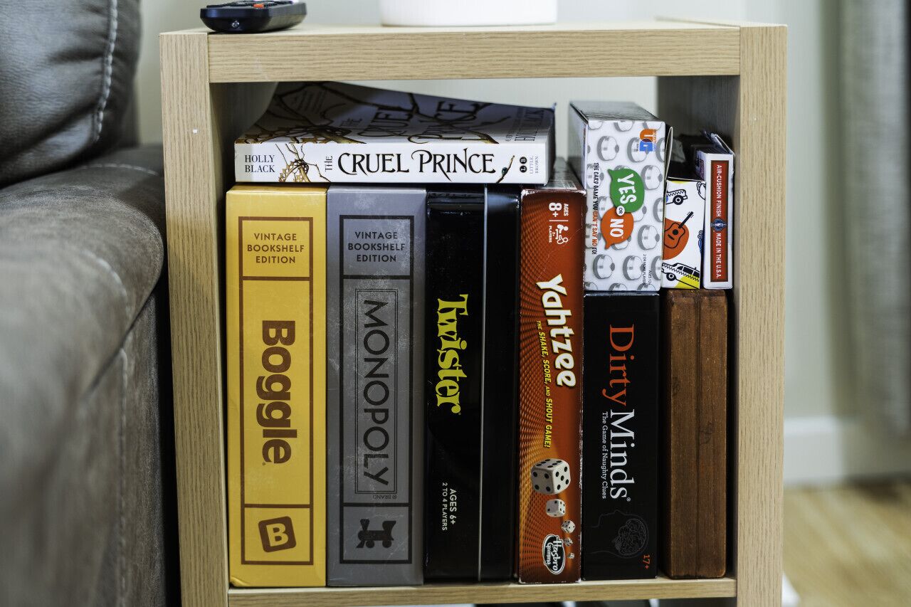 A bookshelf with various books and games, including 'The Cruel Prince,' 'Boggle,' 'Monopoly,' 'Twister,' 'Yacht,' and 'Dirty Minds.'