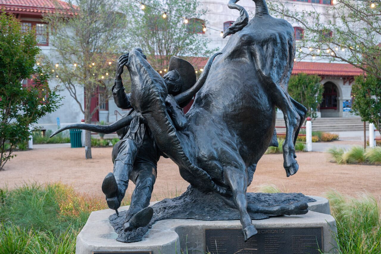 Une statue de bronze représentant un homme et un cheval, située dans un parc.
