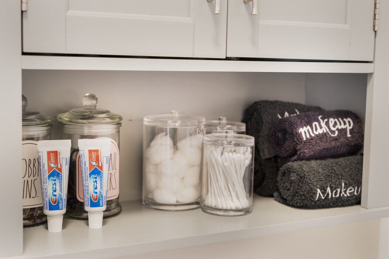 A shelf with jars of cotton balls, cotton swabs, and Crest toothpaste.